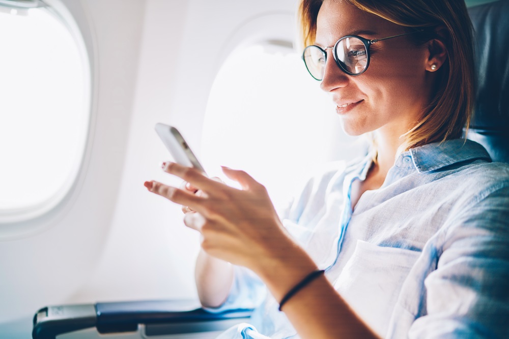 woman on plane looking at phone with glasses