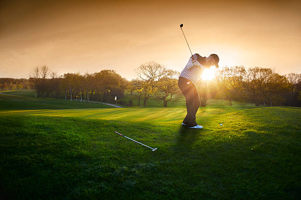 a lone golfer chips onto the green , the low sun is coming from behind him and flaring to camera