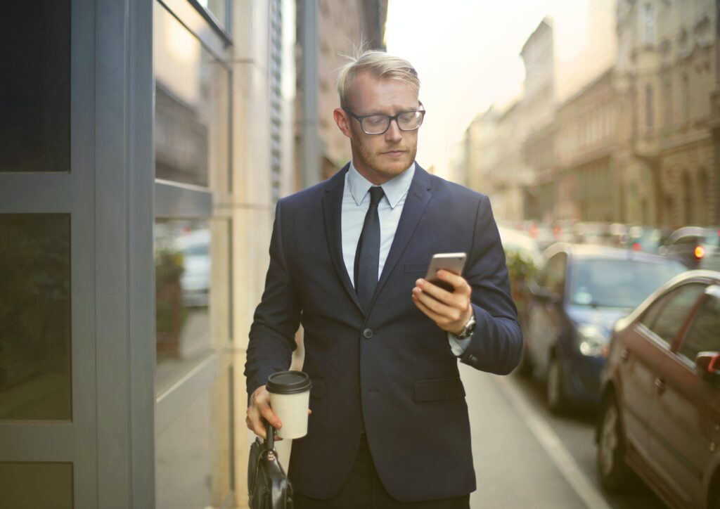 man holding coffee in a dark blue suit looking at the phone
